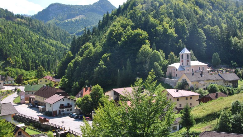 Kleines Dorf in einer grünen Berglandschaft mit Kirche und Häusern.