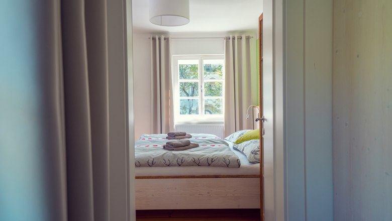 Ein gemütliches Gästezimmer mit Doppelbett, Bettwäsche mit Hirschmotiven und gefalteten Handtüchern auf dem Bett, durch eine offene Tür gesehen.